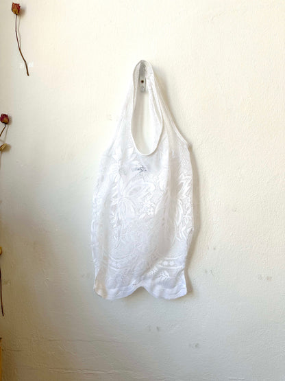 A white lace tote bag with a floral jacquard pattern, hanging on a white wall.