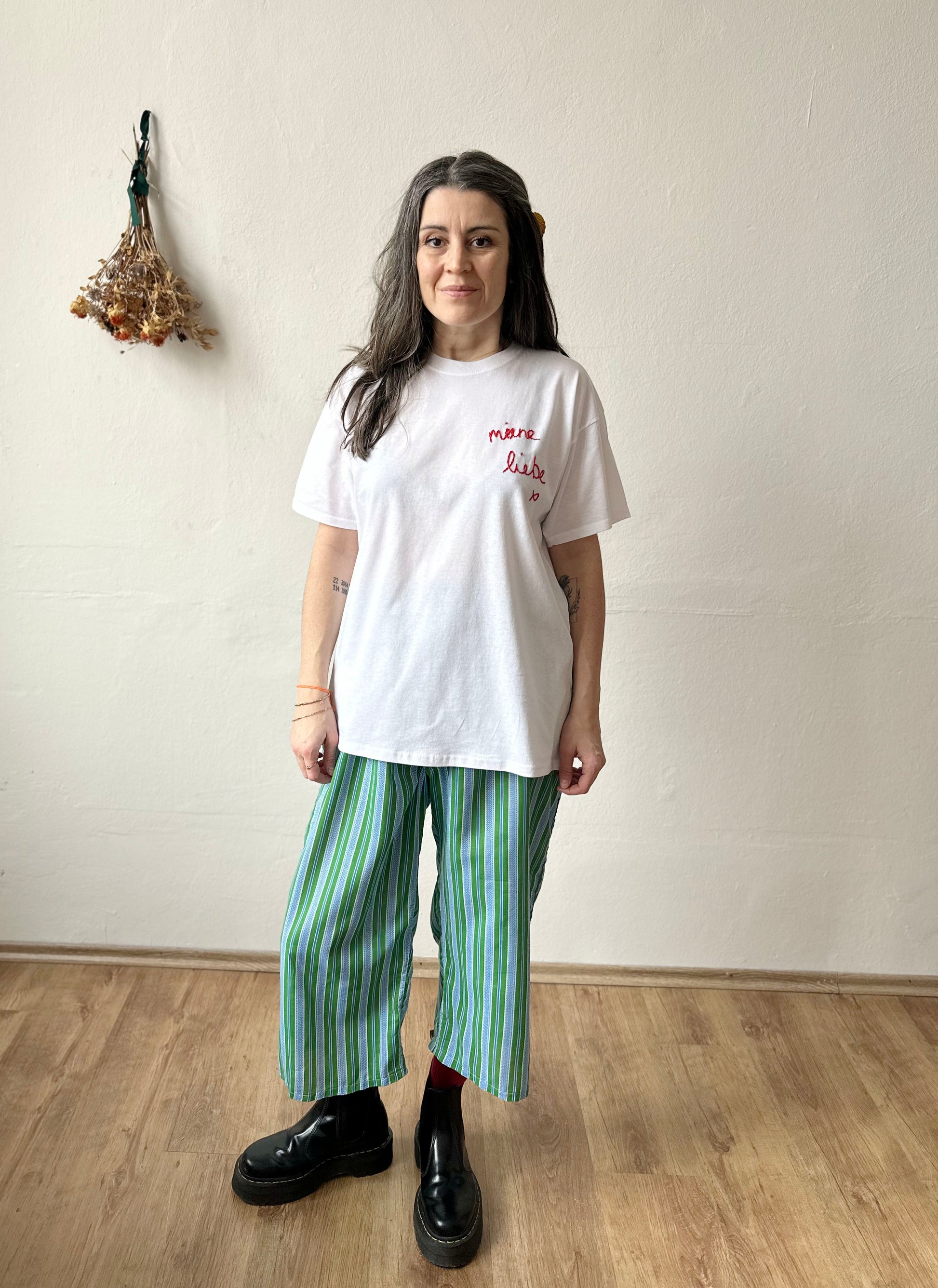 Woman wearing a white embroidered t-shirt with 'Meine Liebe' in red, paired with green striped pants.