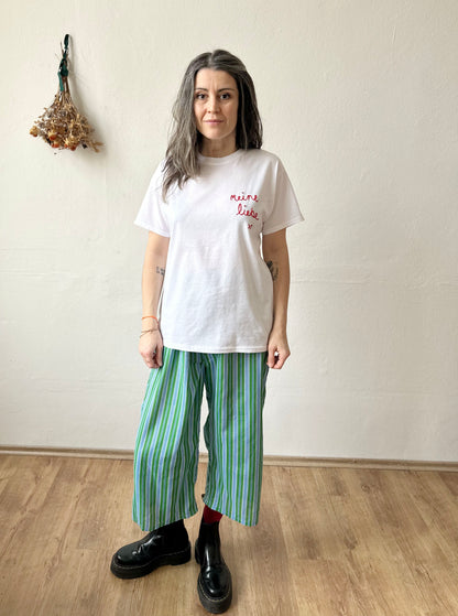 Model wearing Meine Liebe embroidered white t-shirt with green striped pants, showcasing casual style.