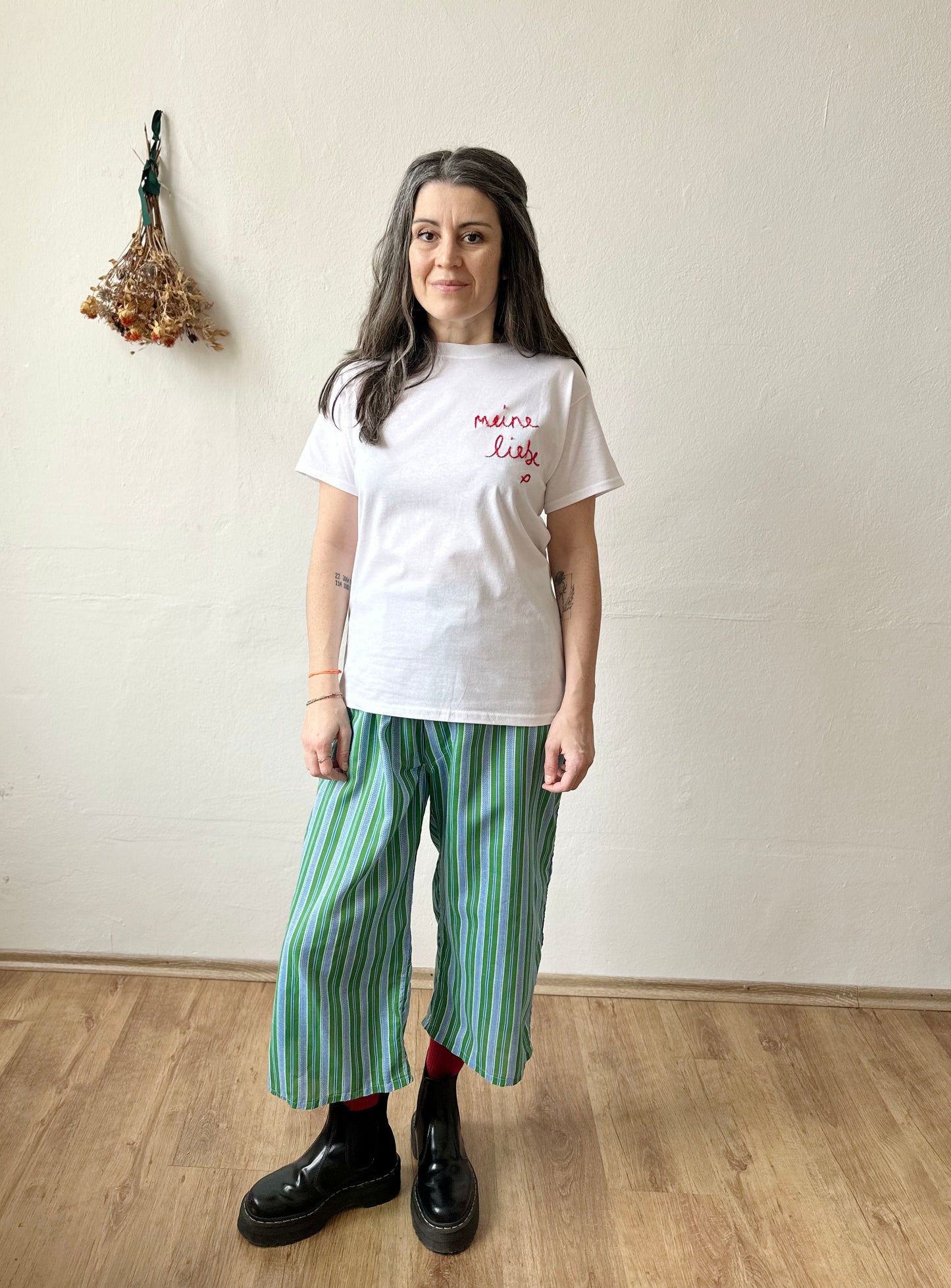 Woman wearing a white t-shirt with 'Meine Liebe' embroidered, paired with striped green pants. Handcrafted in Berlin.