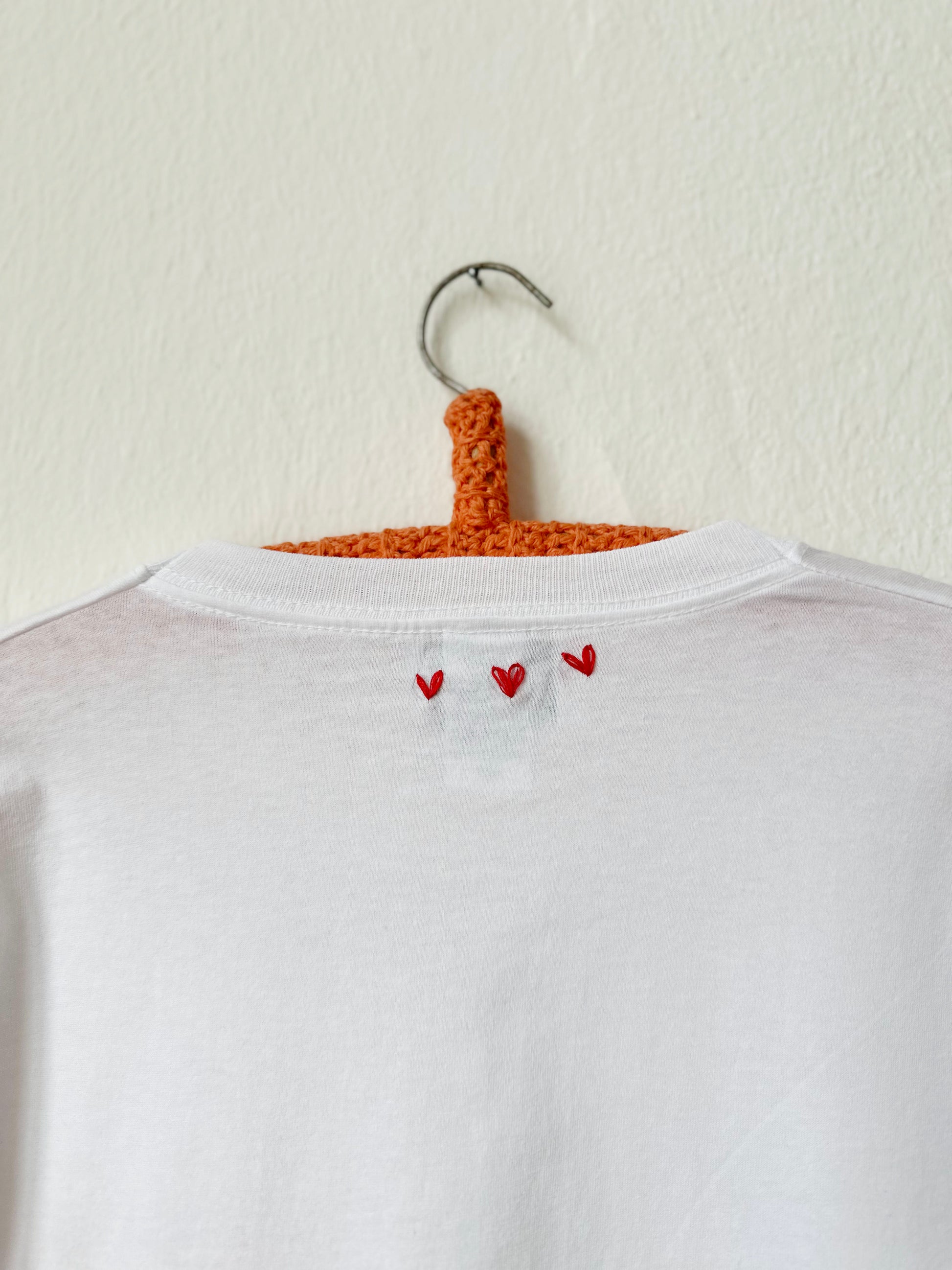 Back view of a white t-shirt with red heart embroidery, showcasing a simple and stylish design.