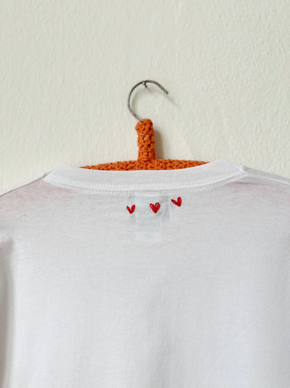 Back view of a white t-shirt with red heart embroidery, showcasing a simple and stylish design.