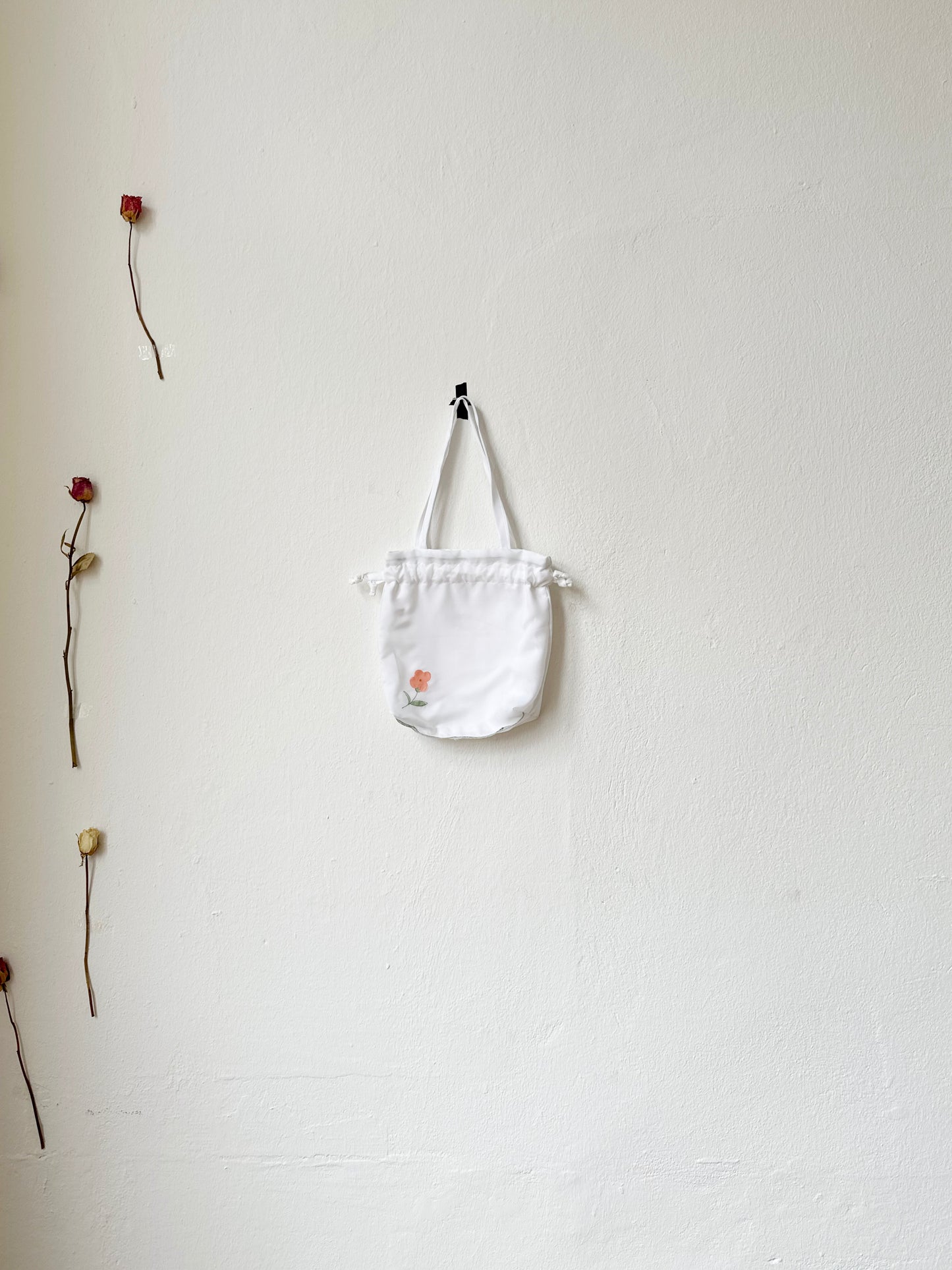 A mini white tote bag with floral pattern hangs on a wall.