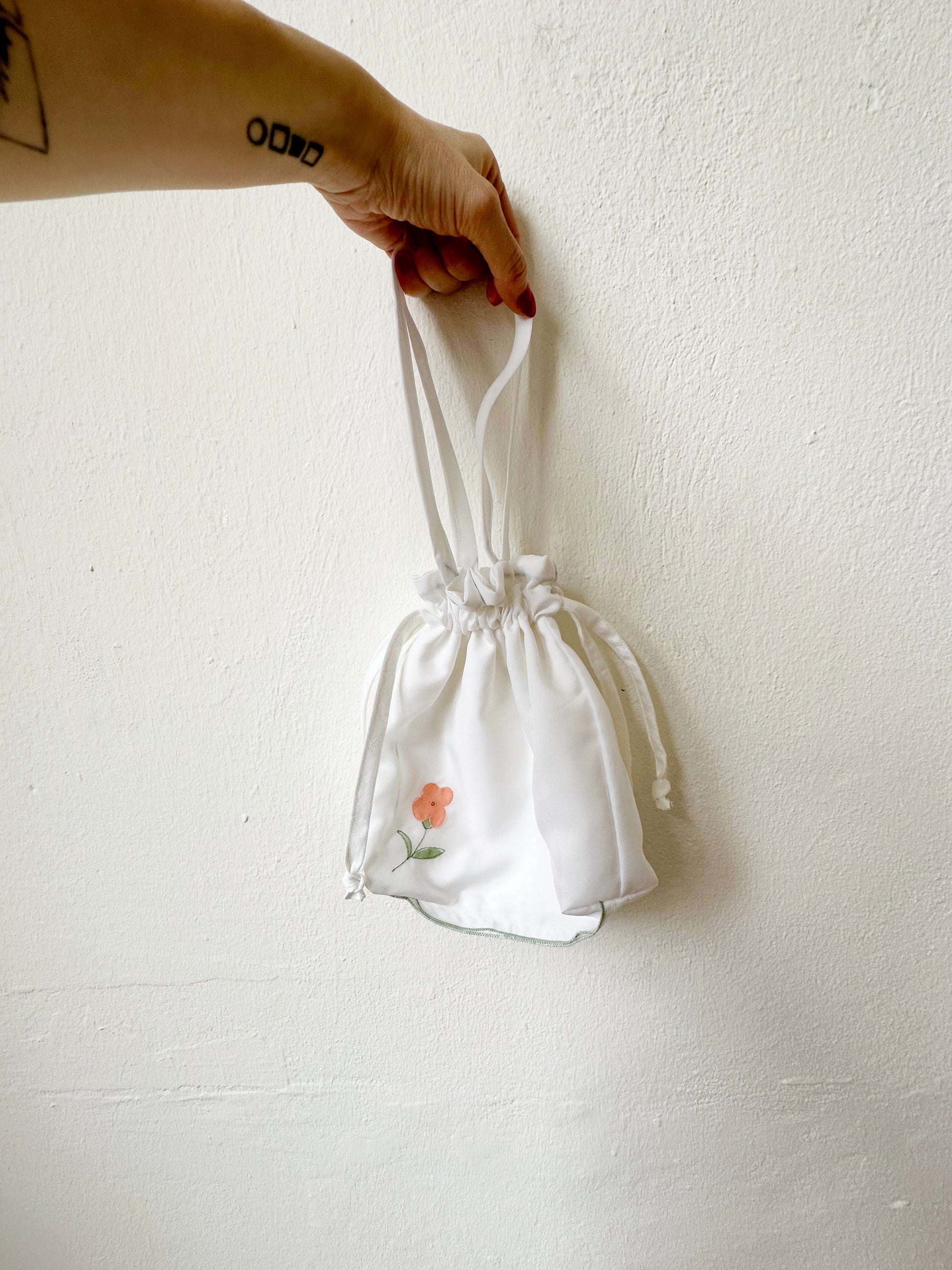 A small hand bag in white with floral design against a wall.