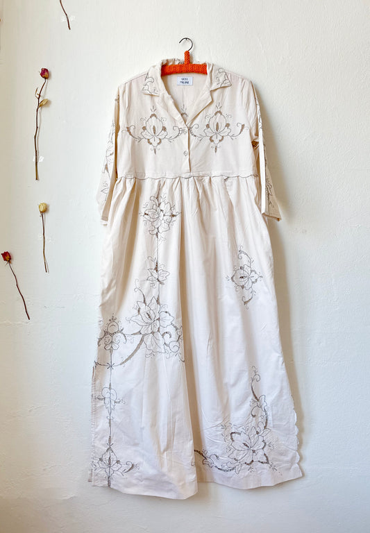 The front view of a maxi length grey embroidered dress hanging on a wall.