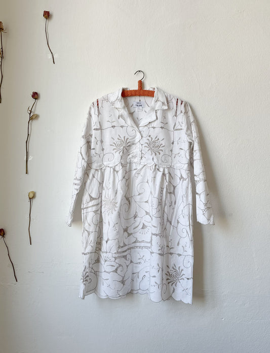 A white and grey embroidered lace dress hanging on a wall.