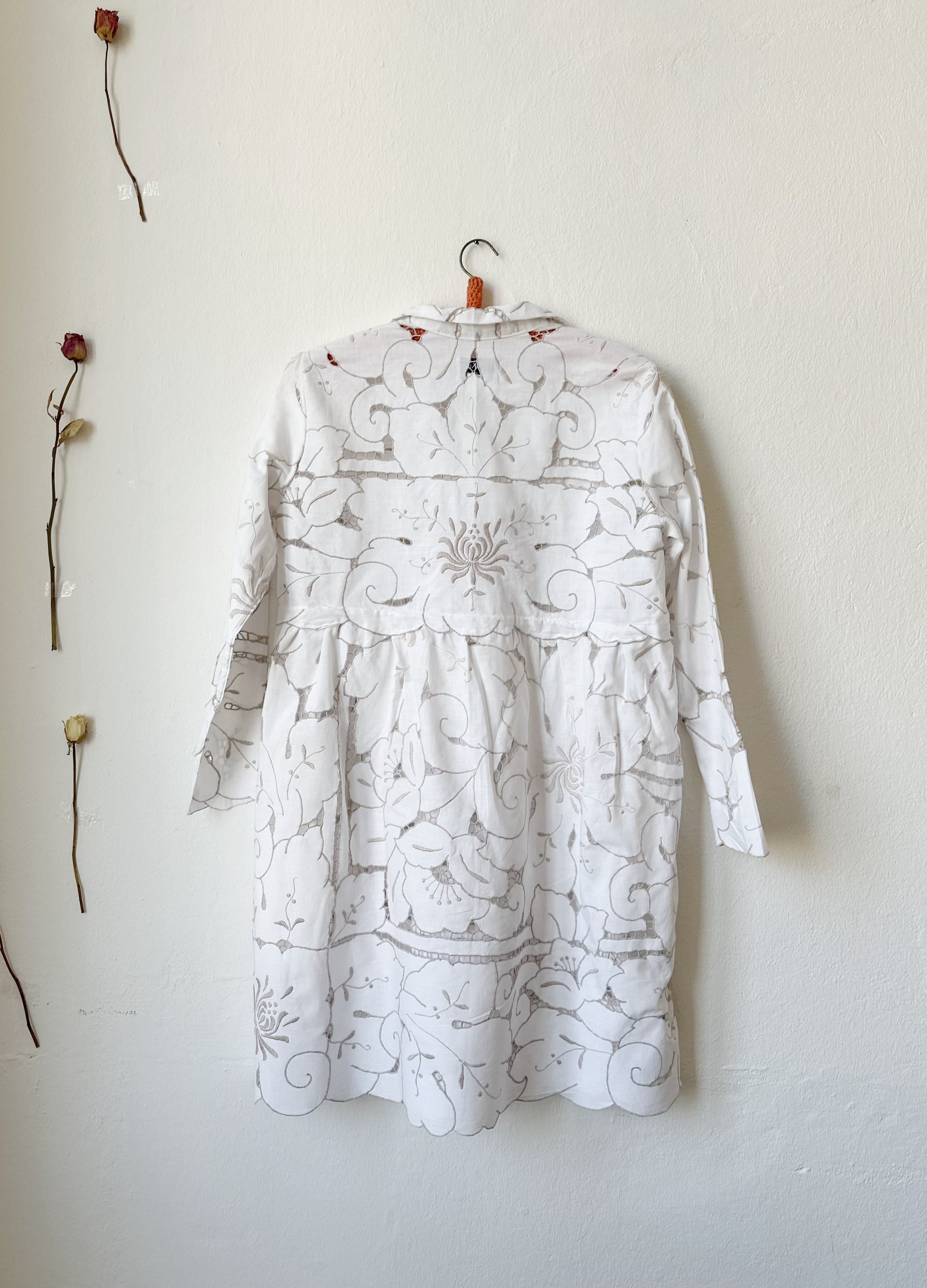 The back view of a white and grey embroidered dress hanging on a wall