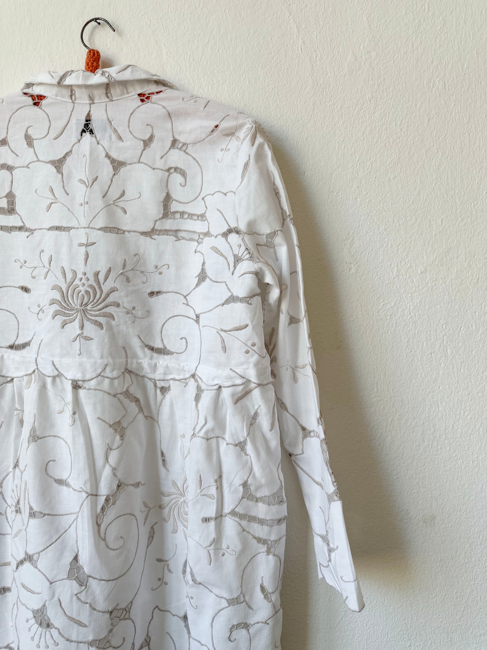 A detailed back view of a white and grey embroidered lace dress hanging on a wall.