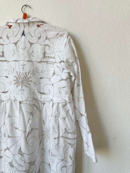 A detailed back view of a white and grey embroidered lace dress hanging on a wall.