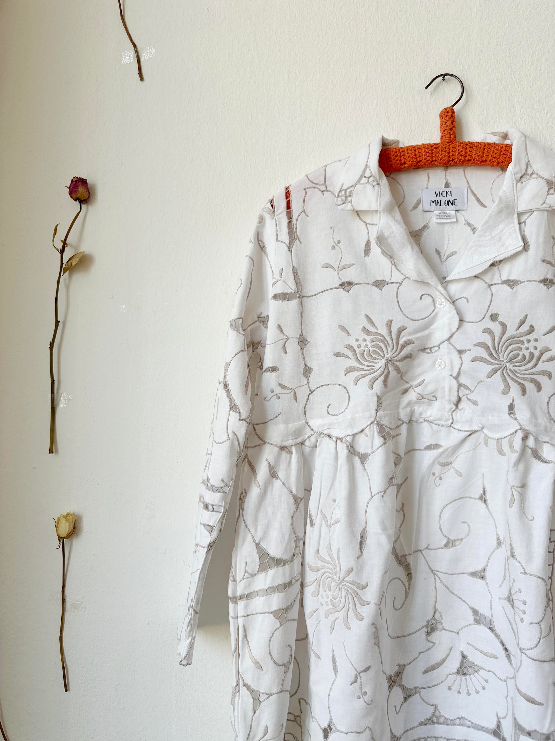 A detailed front view of a white and grey embroidered lace dress hanging on a wall