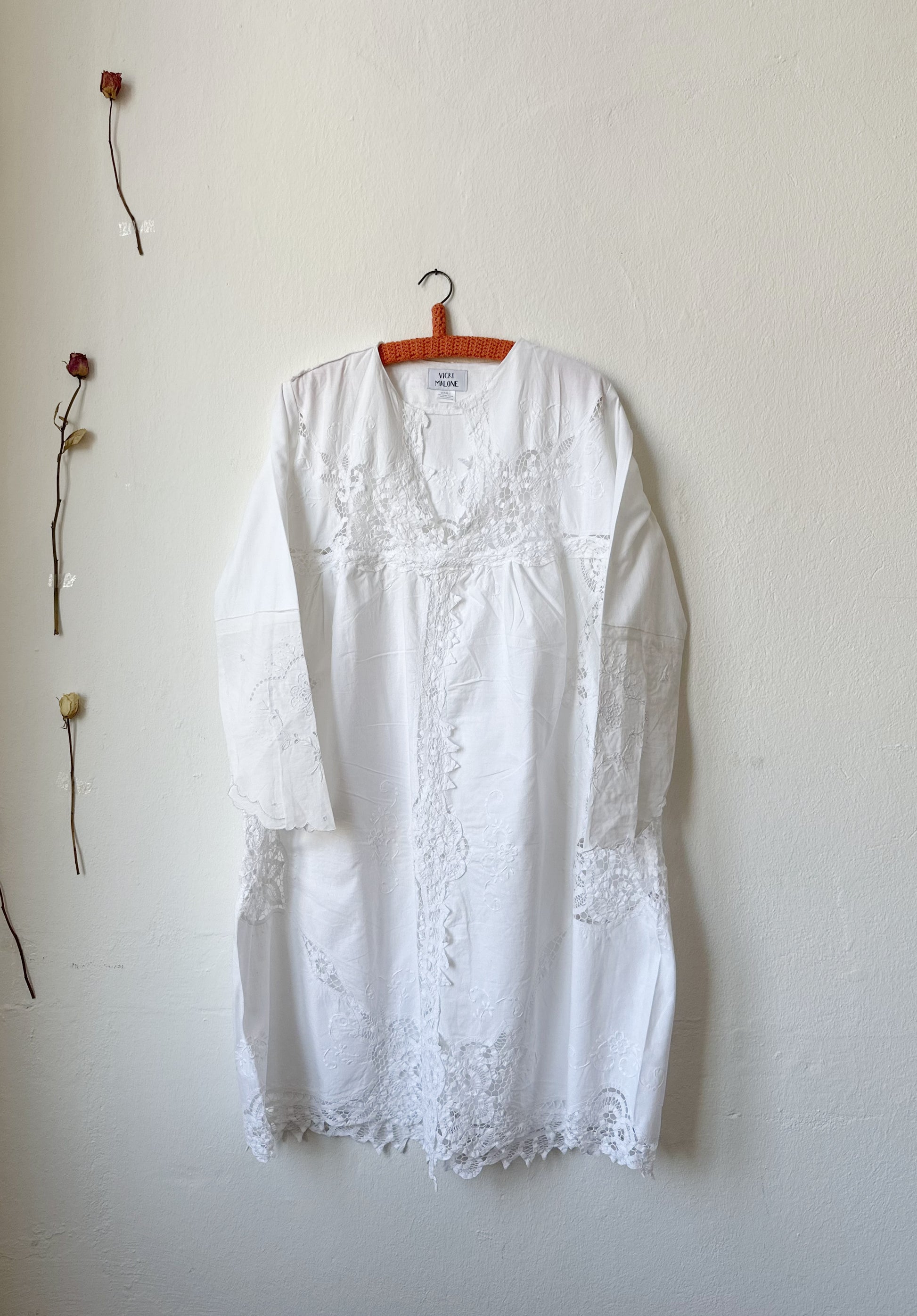A white lace dress hanging on a wall.