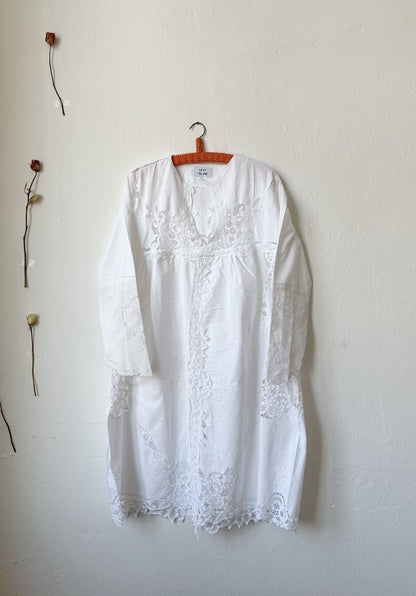 A white lace dress hanging on a wall.