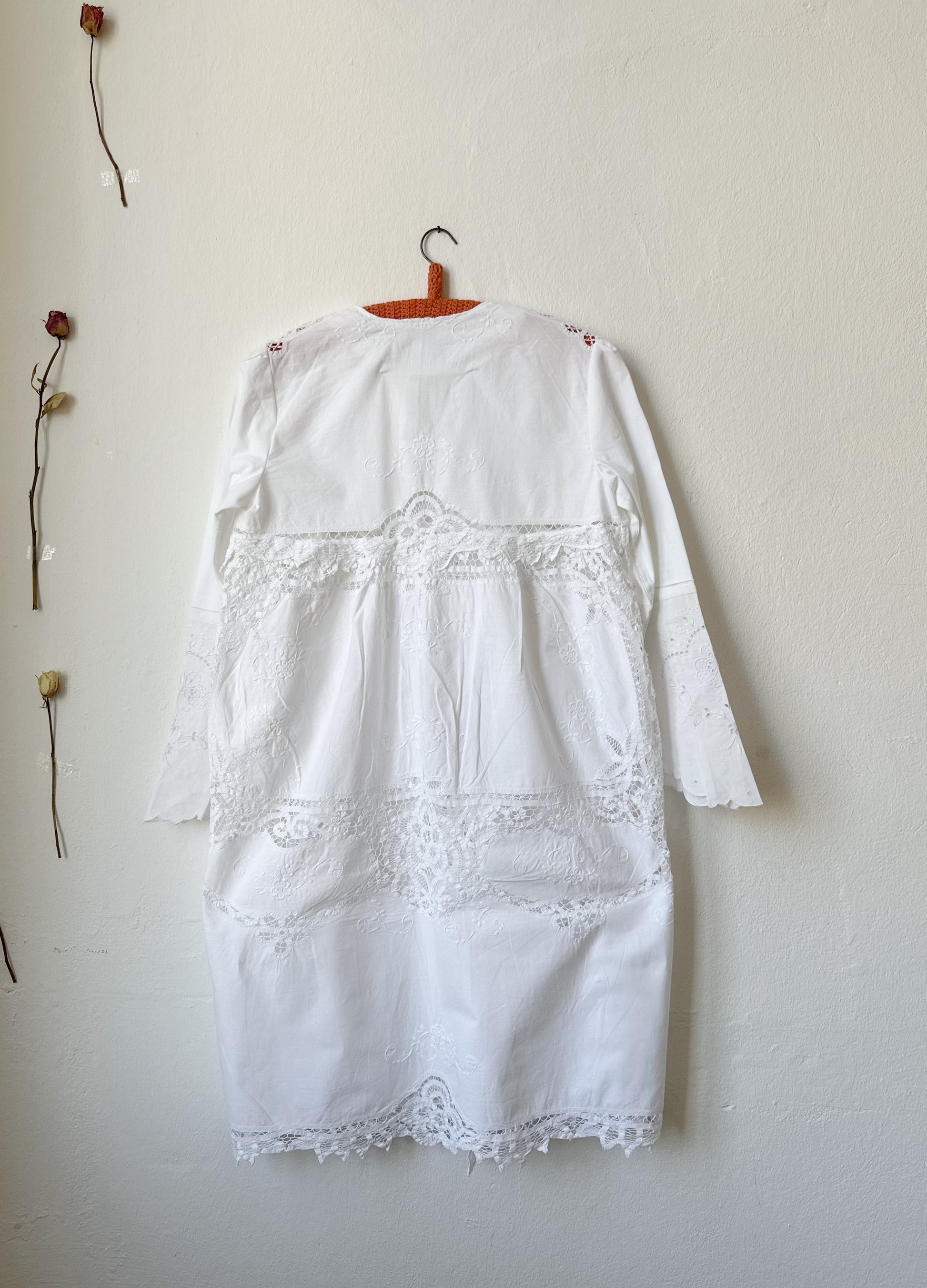 The back of a white lace dress hanging on a wall.