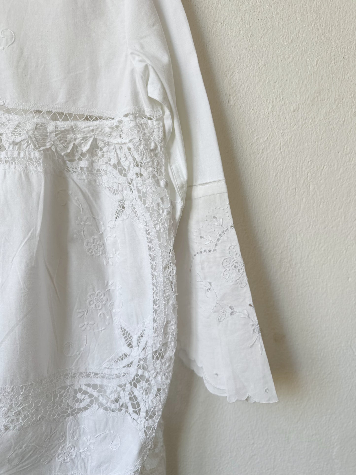 A detailed view of the lace at theback of a white lace dress hanging on a wall.