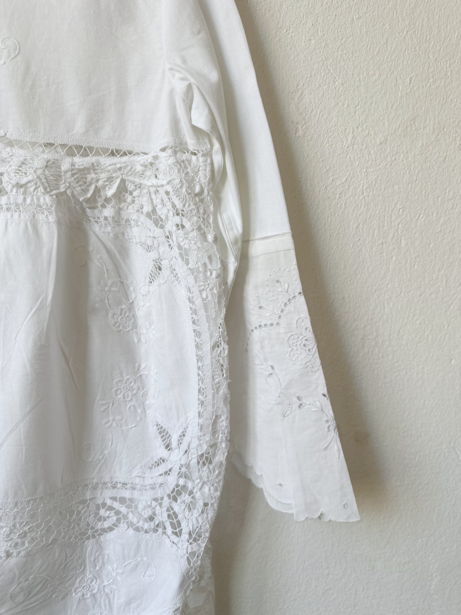 A detailed view of the lace at theback of a white lace dress hanging on a wall.