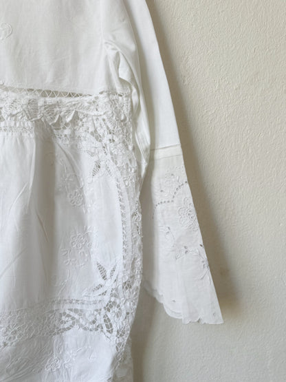 A detailed view of the lace at theback of a white lace dress hanging on a wall.