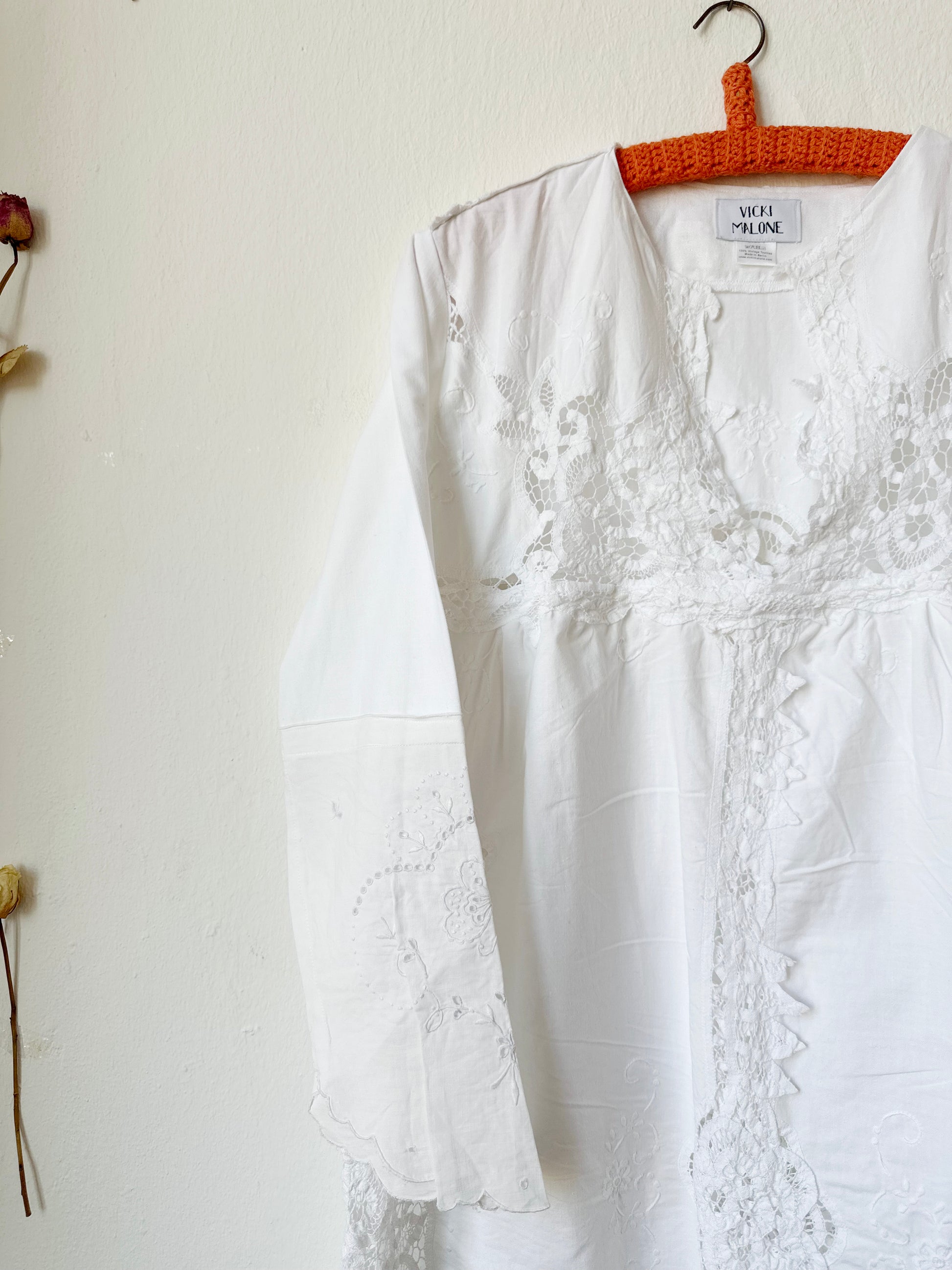 A detailed view of the front of a white lace dress hanging on a wall.