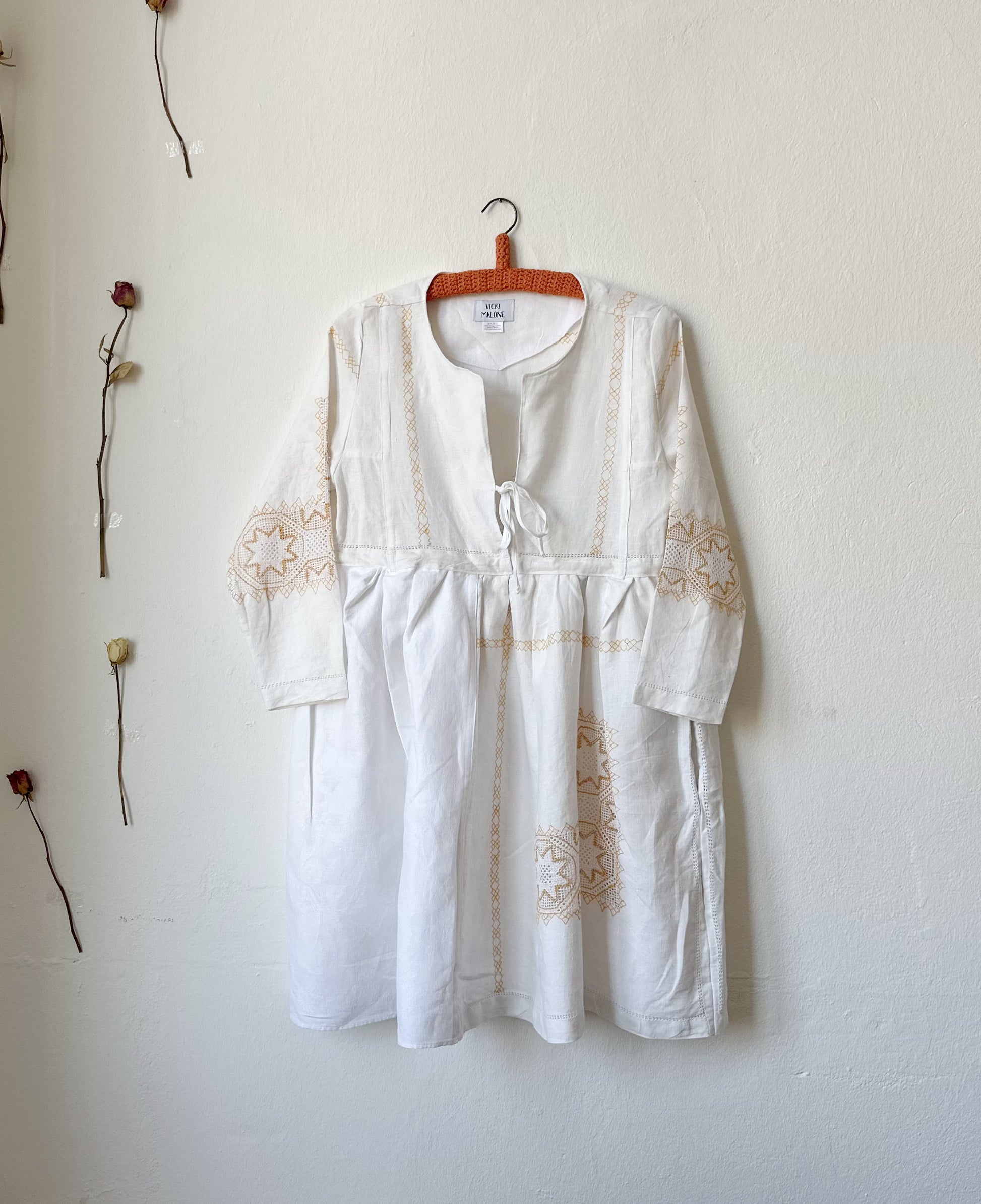 The front view of a white dress with yellow embroidery hanging on a wall