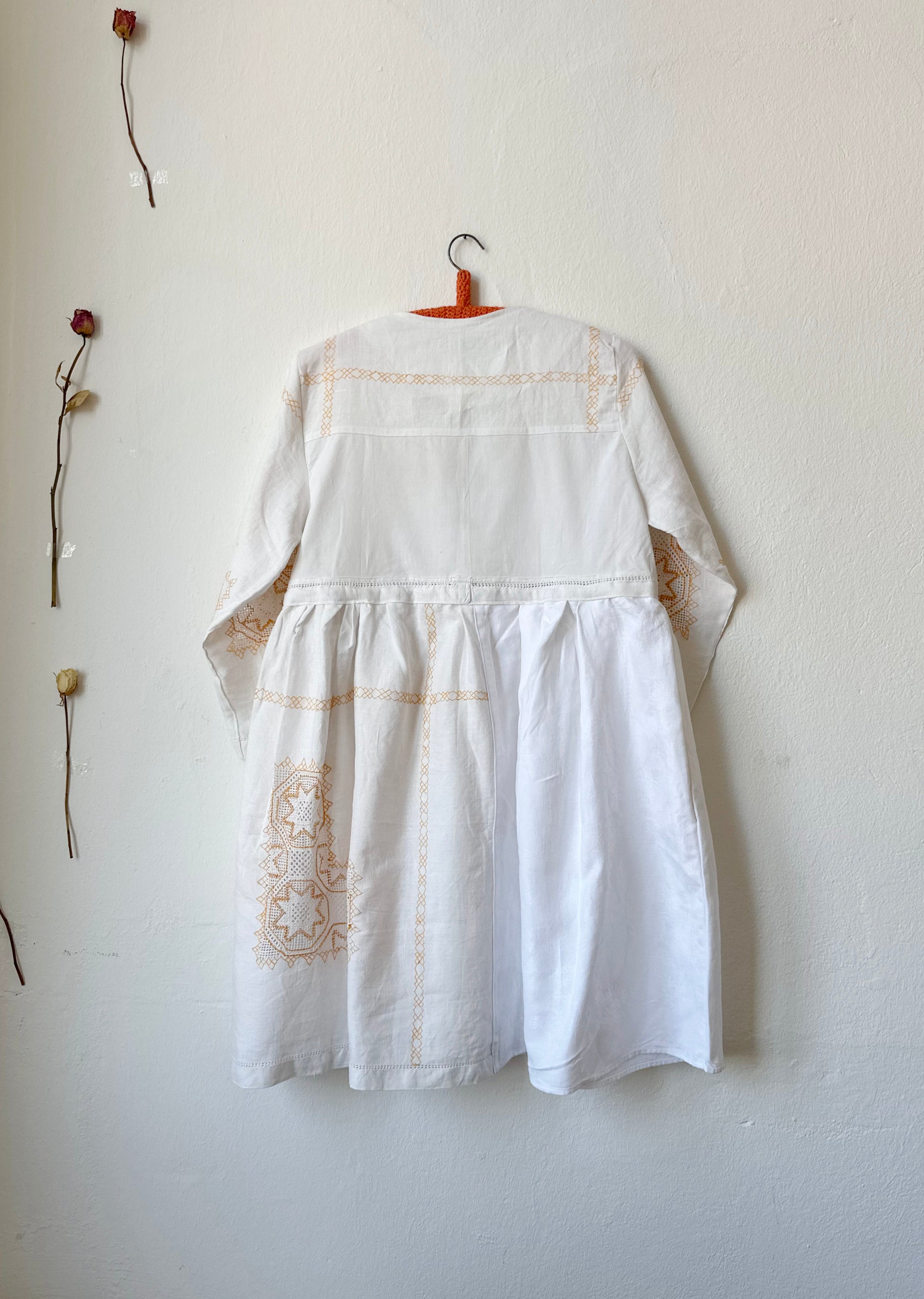 The back view of a white dress with yellow embroidery hanging on a wall