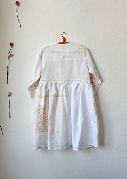 The back view of a white dress with yellow embroidery hanging on a wall