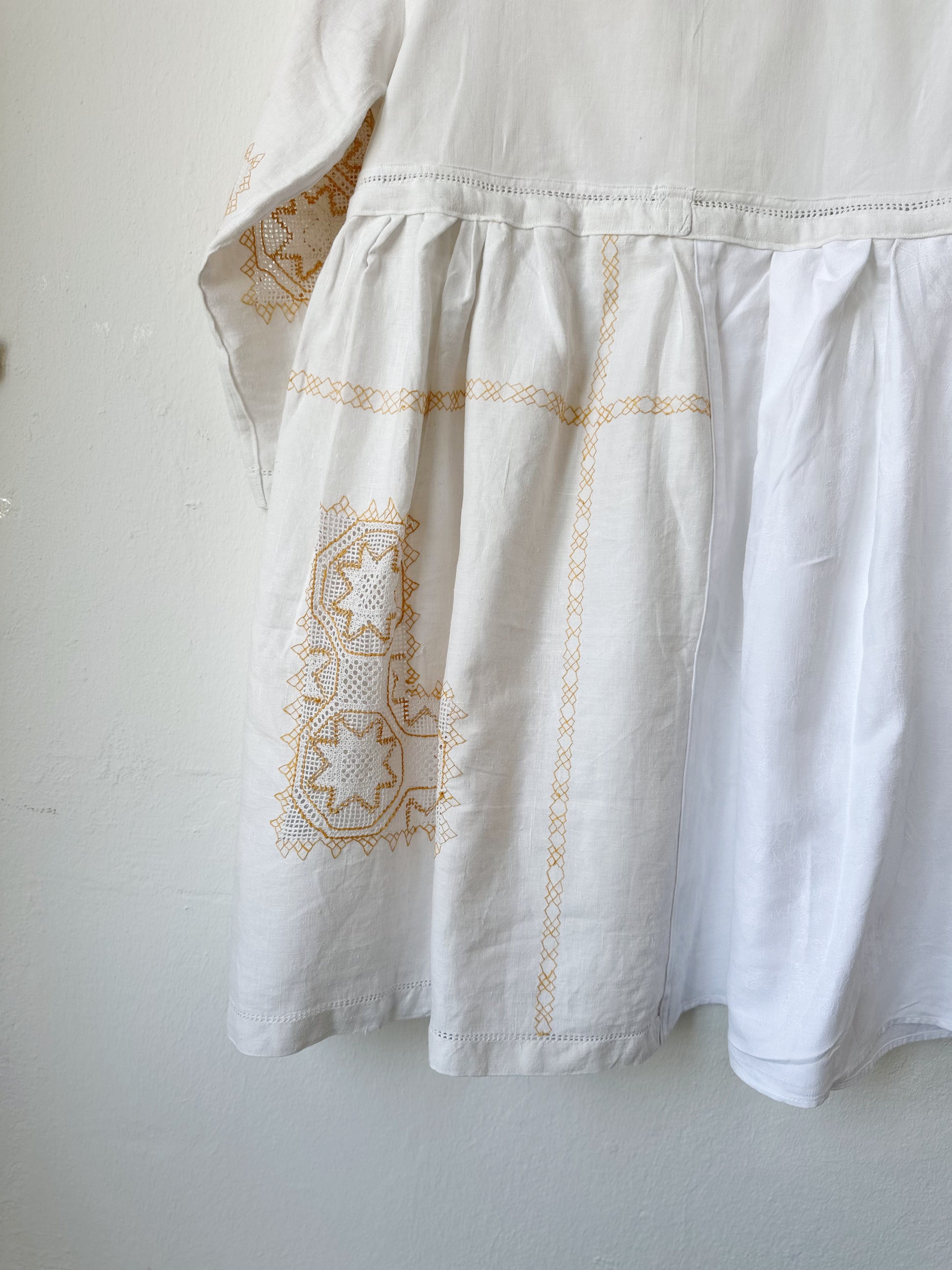 A detailed back view of a white dress with yellow embroidery
