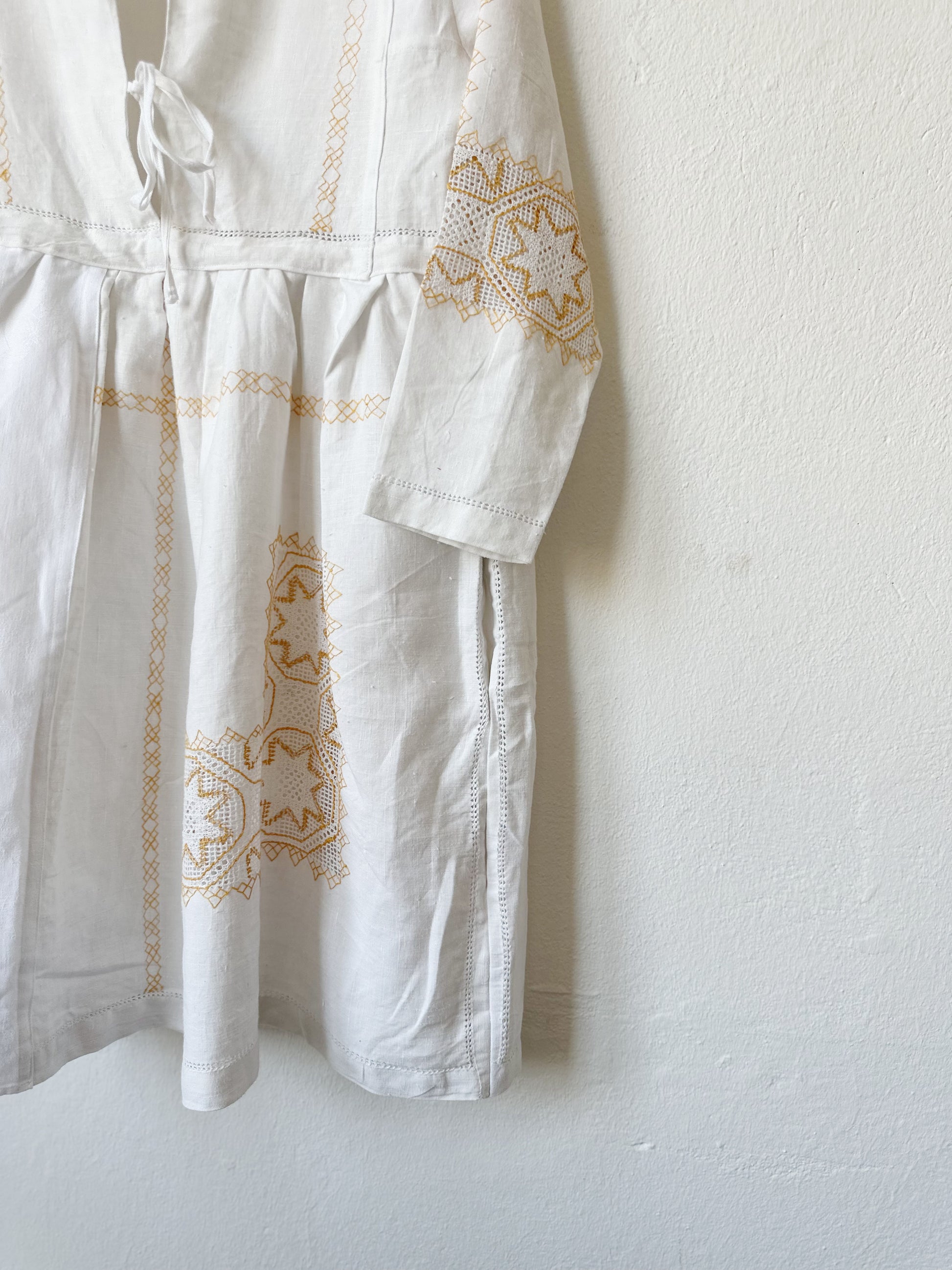 A detailed front view of a white dress with yellow embroidery