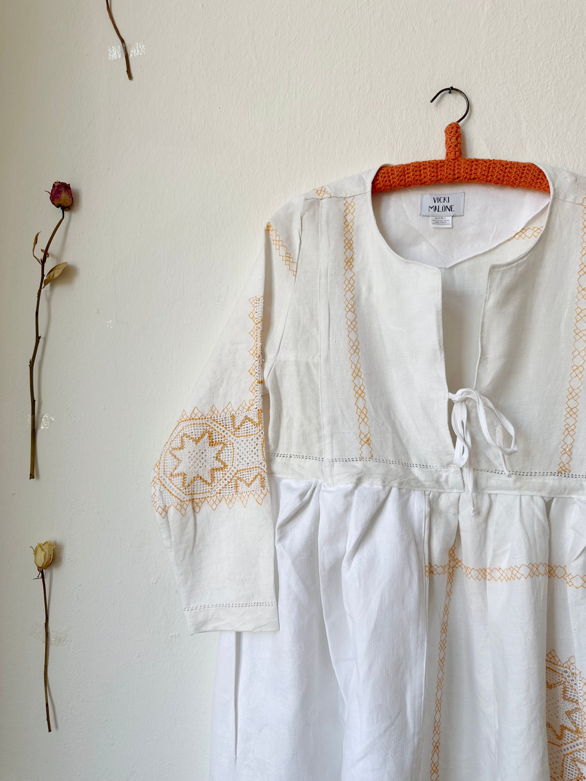The front detail view of a white dress with yellow embroidery hanging on a wall