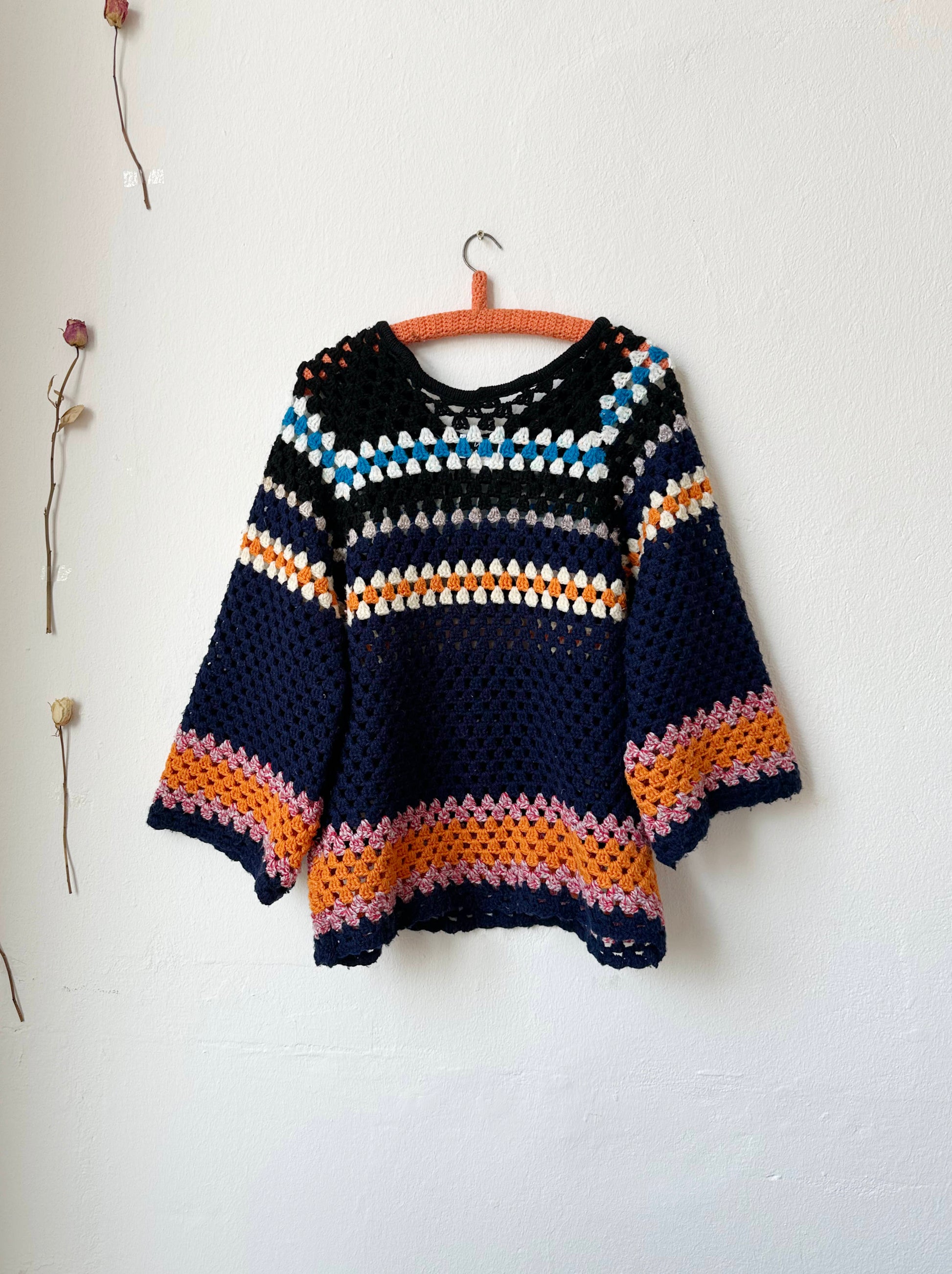 The back view of a navy striped crochet sweater hanging on a wall
