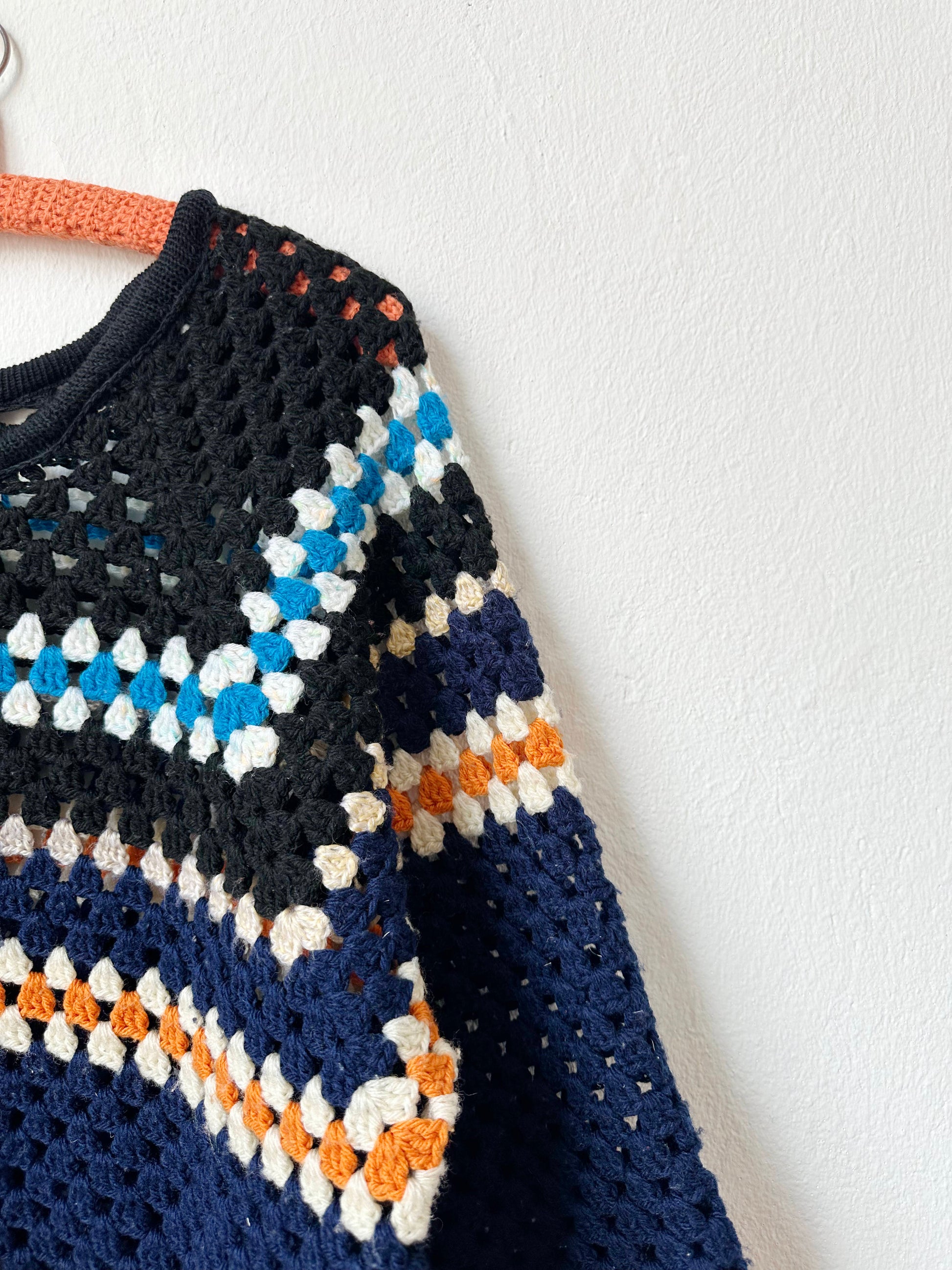 A shoulder detail view of a navy striped sweater hanging on a wall
