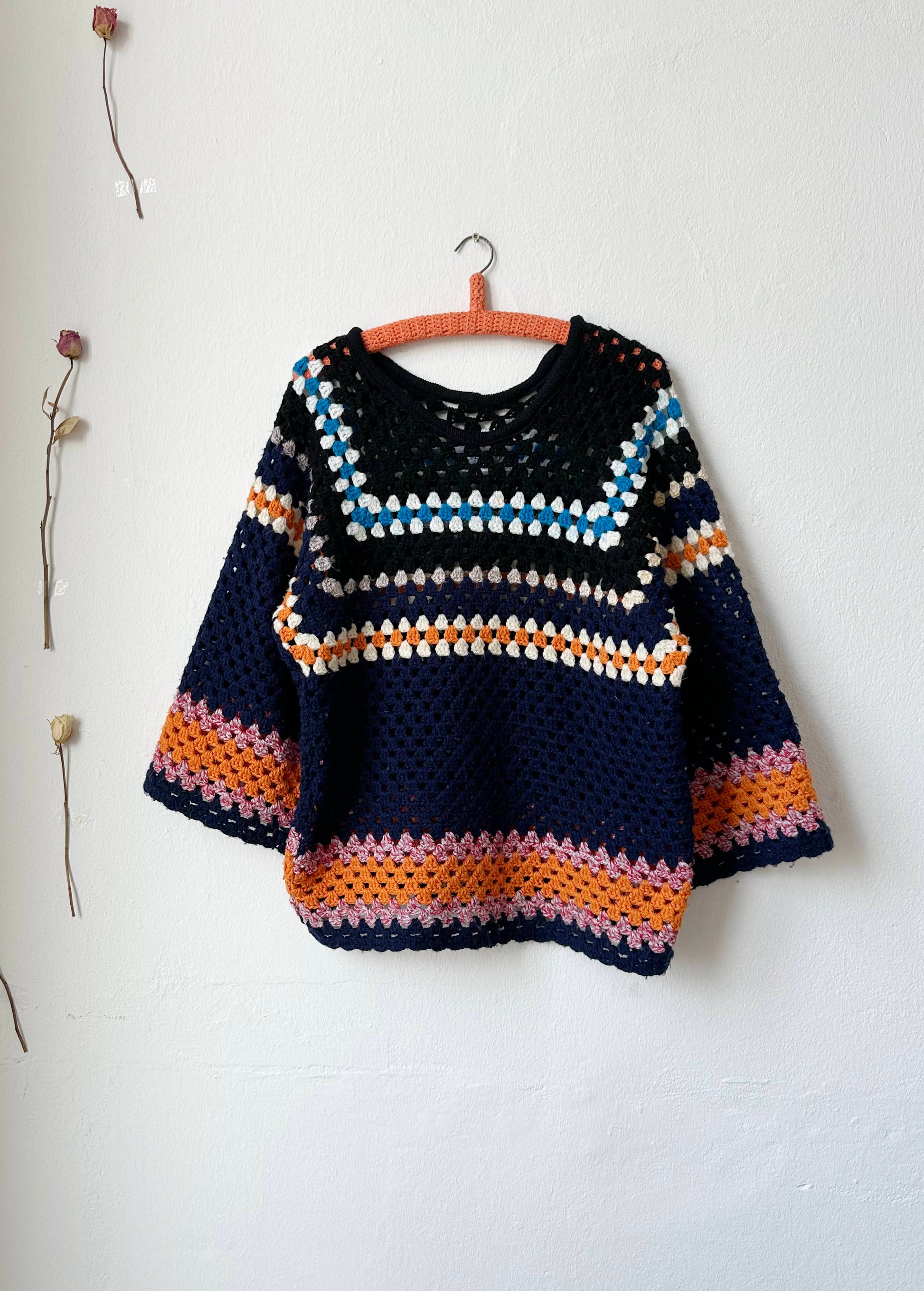 A navy striped crochet sweater hanging on a wall