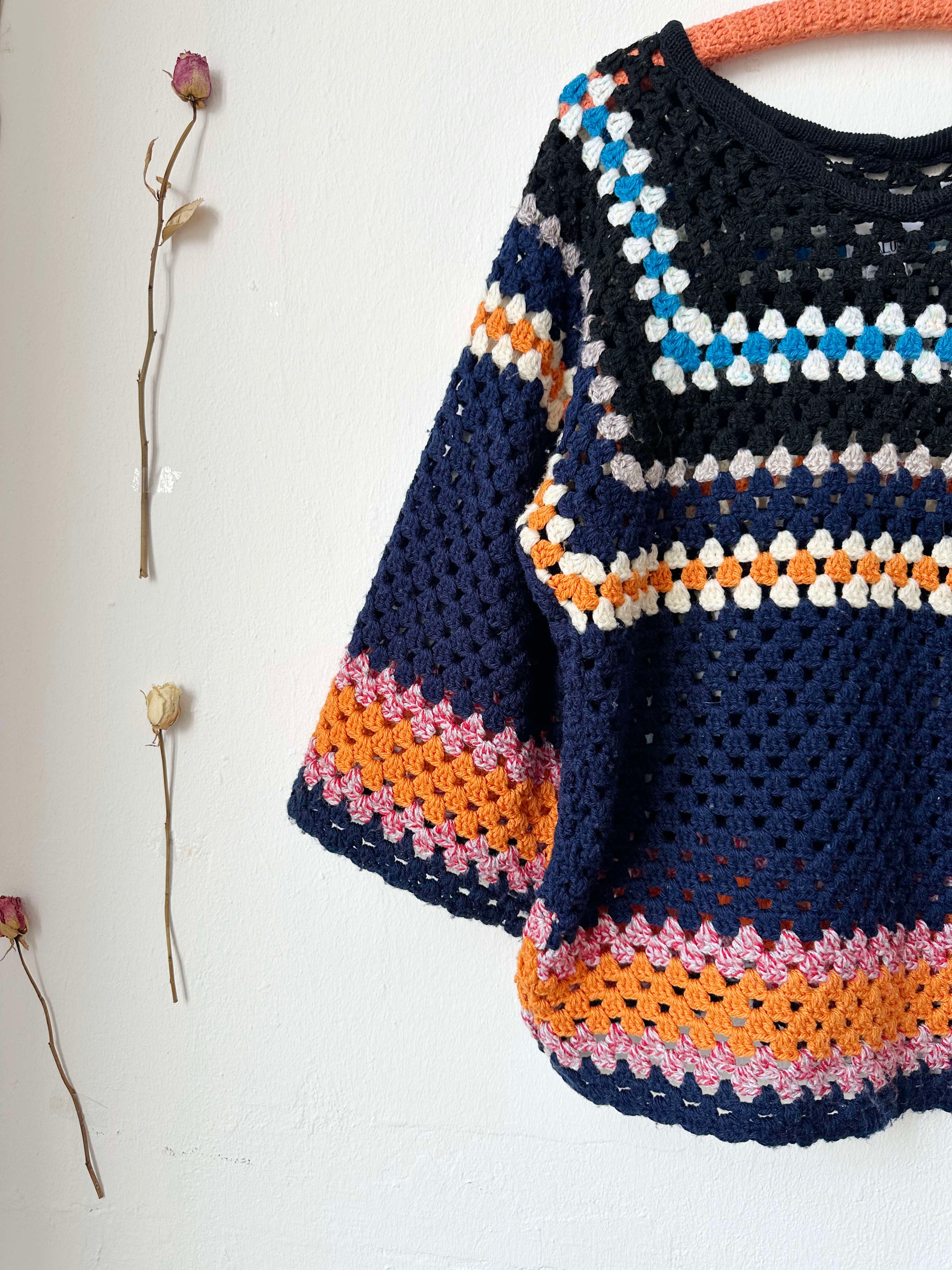 A front detailed view of a navy striped crochet sweater hanging on a wall