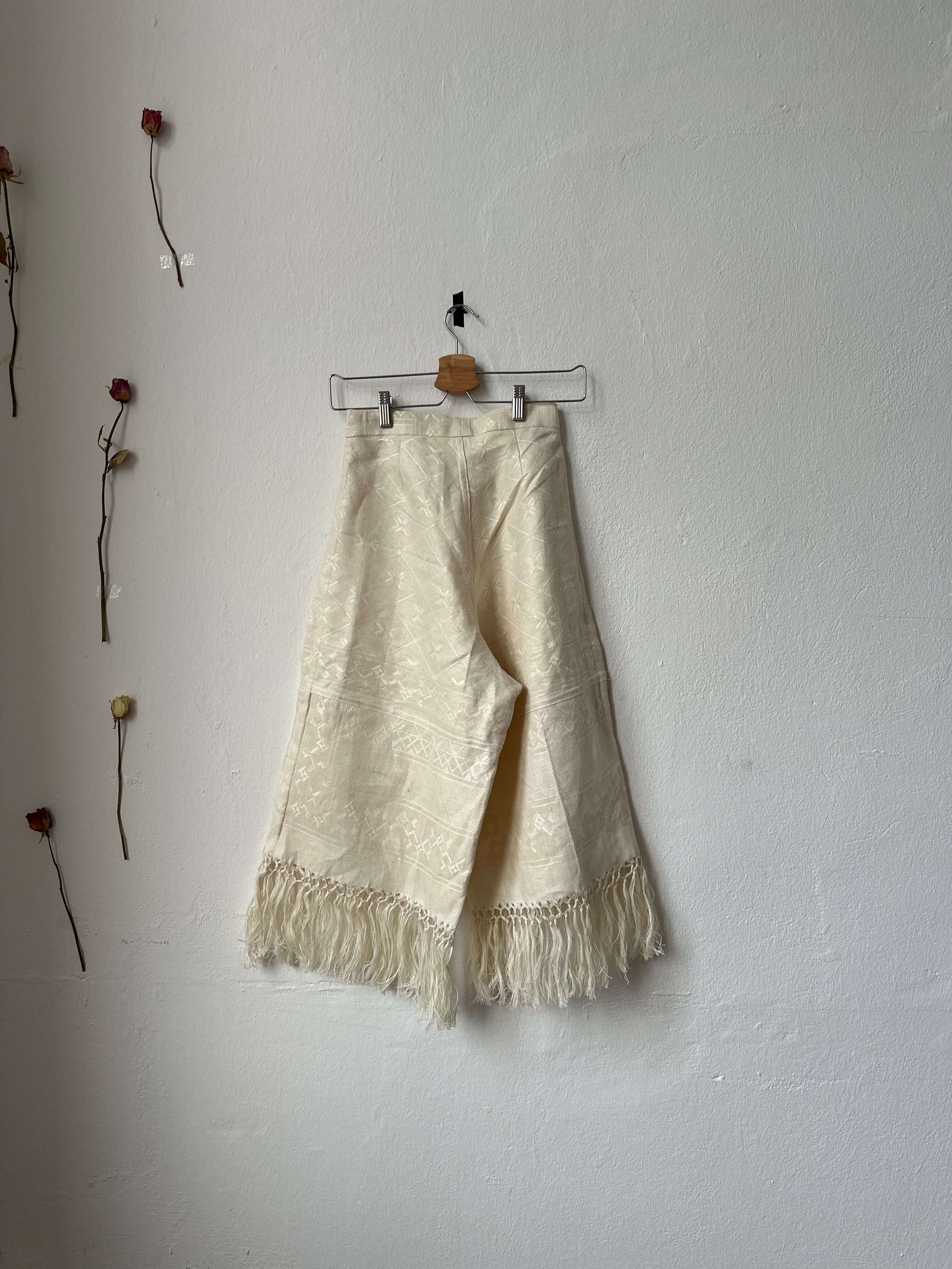 Back view of wide leg, high waist trousers hanging on a wall.
