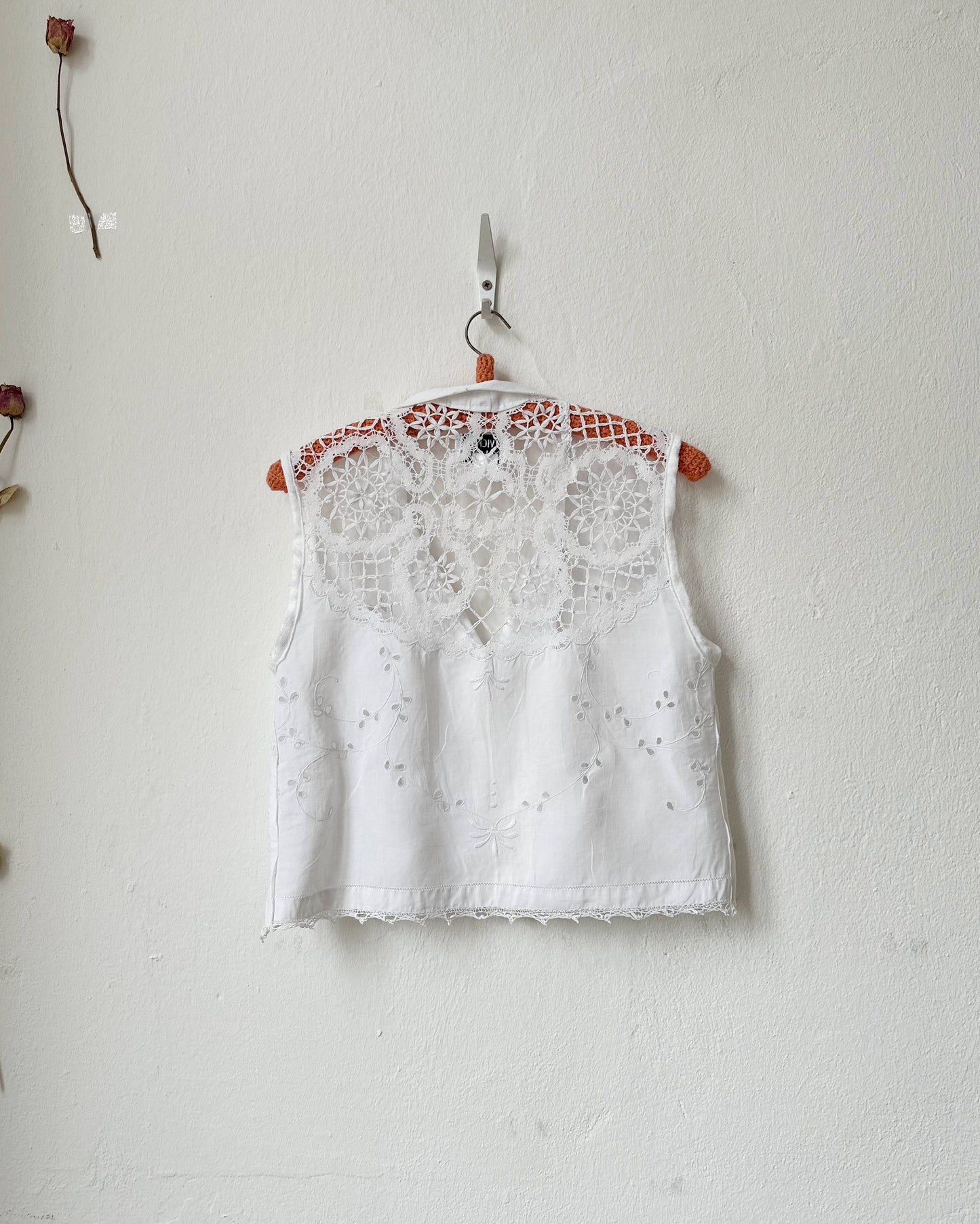White lace top hanging on a white wall with a small branch and flower decorations.