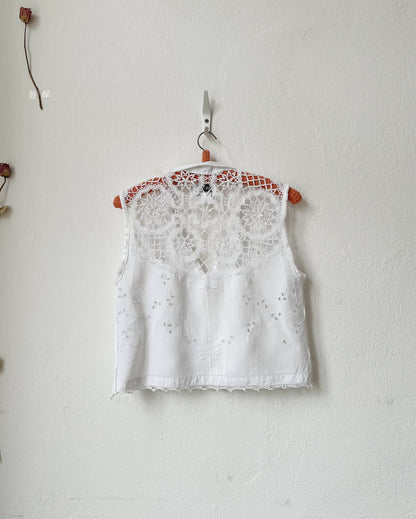 White lace top hanging on a white wall with a small branch and flower decorations.