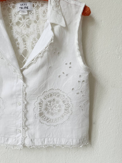 White embroidered vest with lace details on a white background
