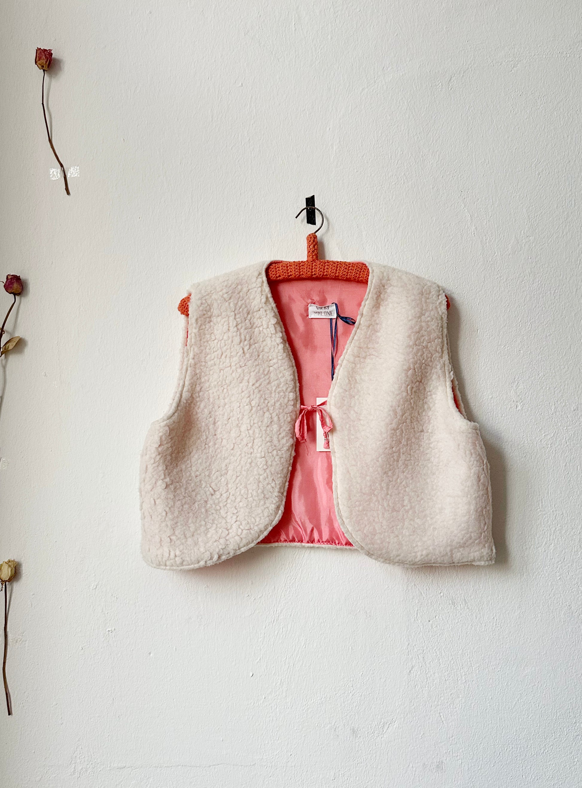 A front view of a mock shearling vem vest with pink lining hanging on a wall.