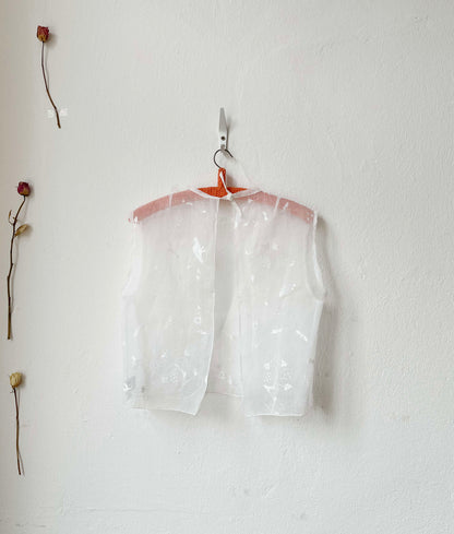 Sheer embroidered vest top on a hanger against a white wall with dried flowers.