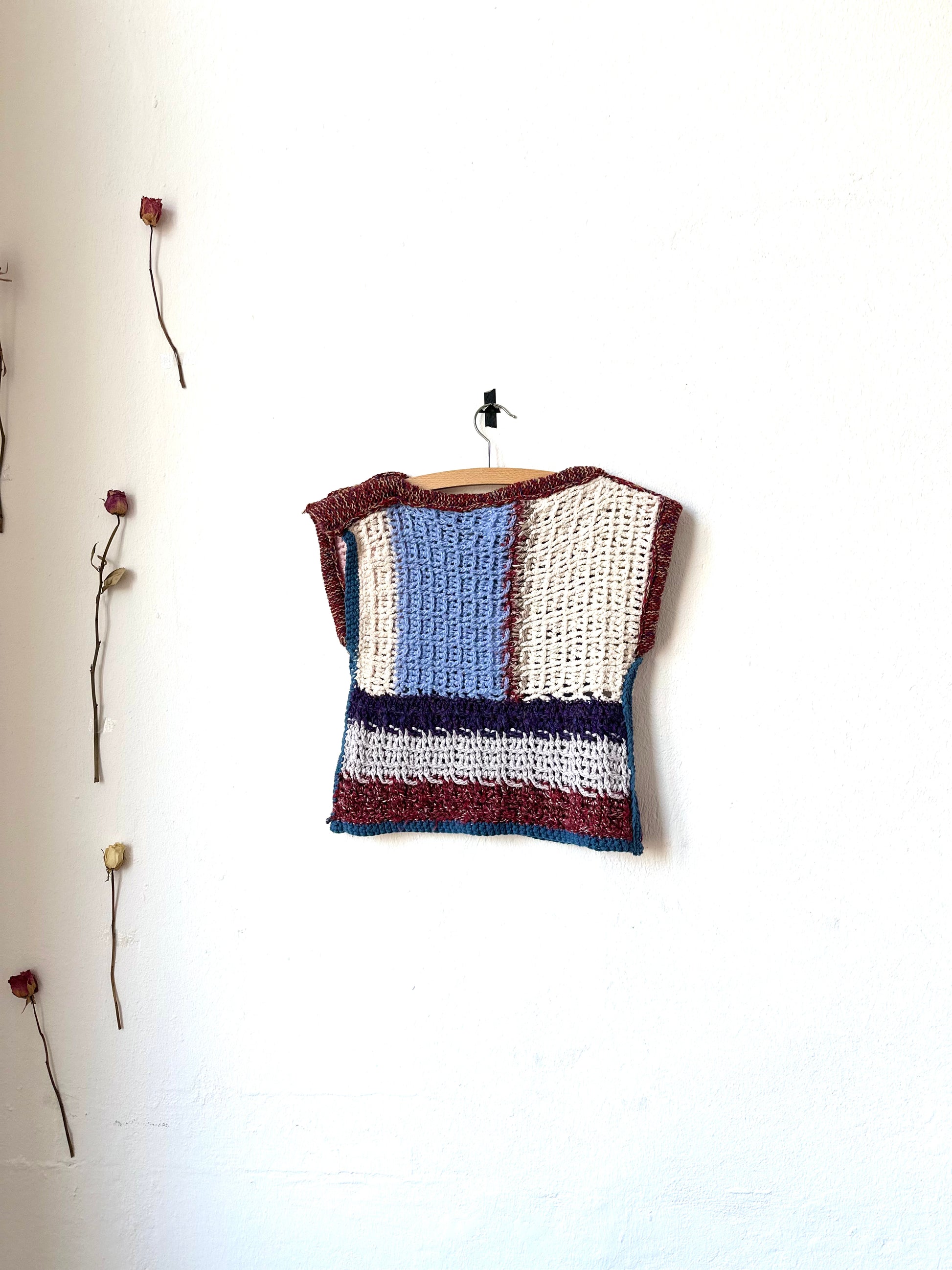 View of a crochet blanket vest hanging on a wall.