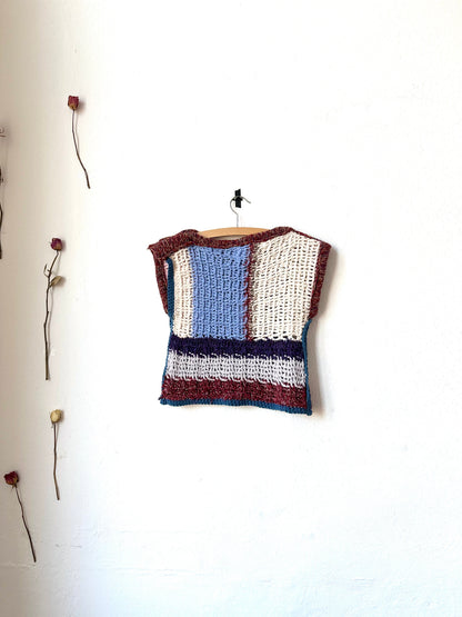 View of a crochet blanket vest hanging on a wall.