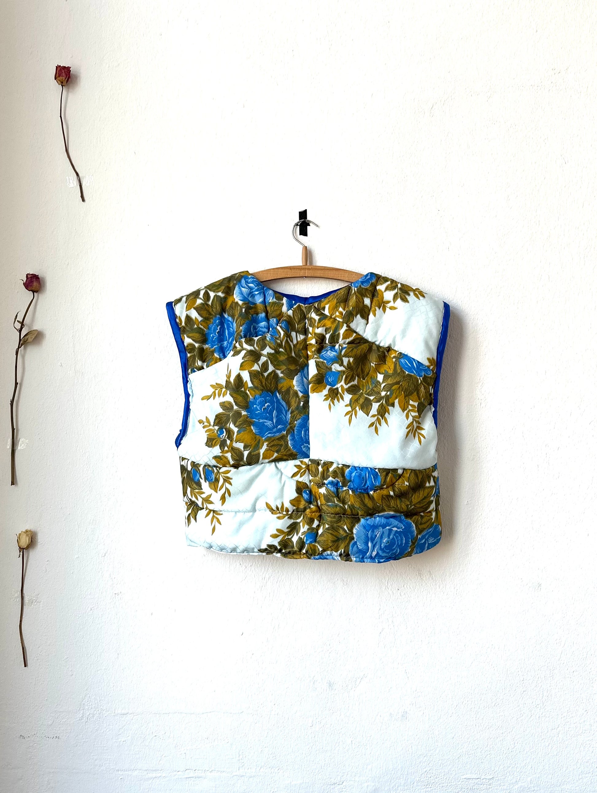 A rear view of blue floral quilted vest hanging on a wall.