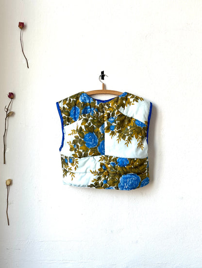 A rear view of blue floral quilted vest hanging on a wall.