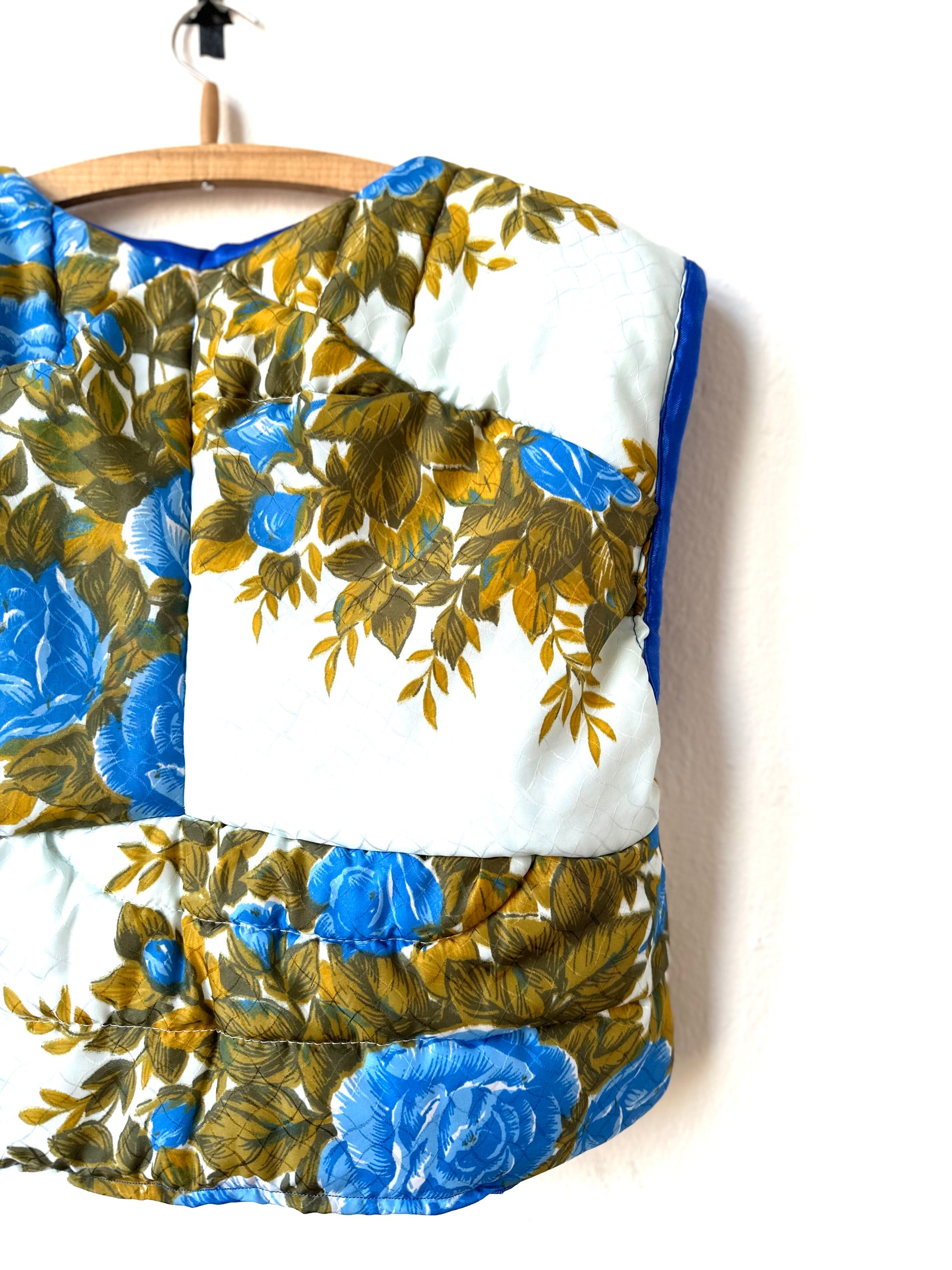 A rear view of blue floral quilted vest hanging on a wall.