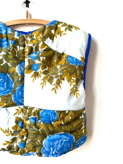 A rear view of blue floral quilted vest hanging on a wall.