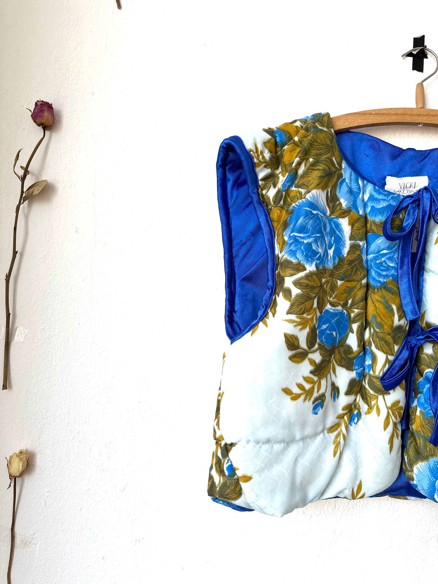 A blue floral quilt vest with ties hangs on a wall.