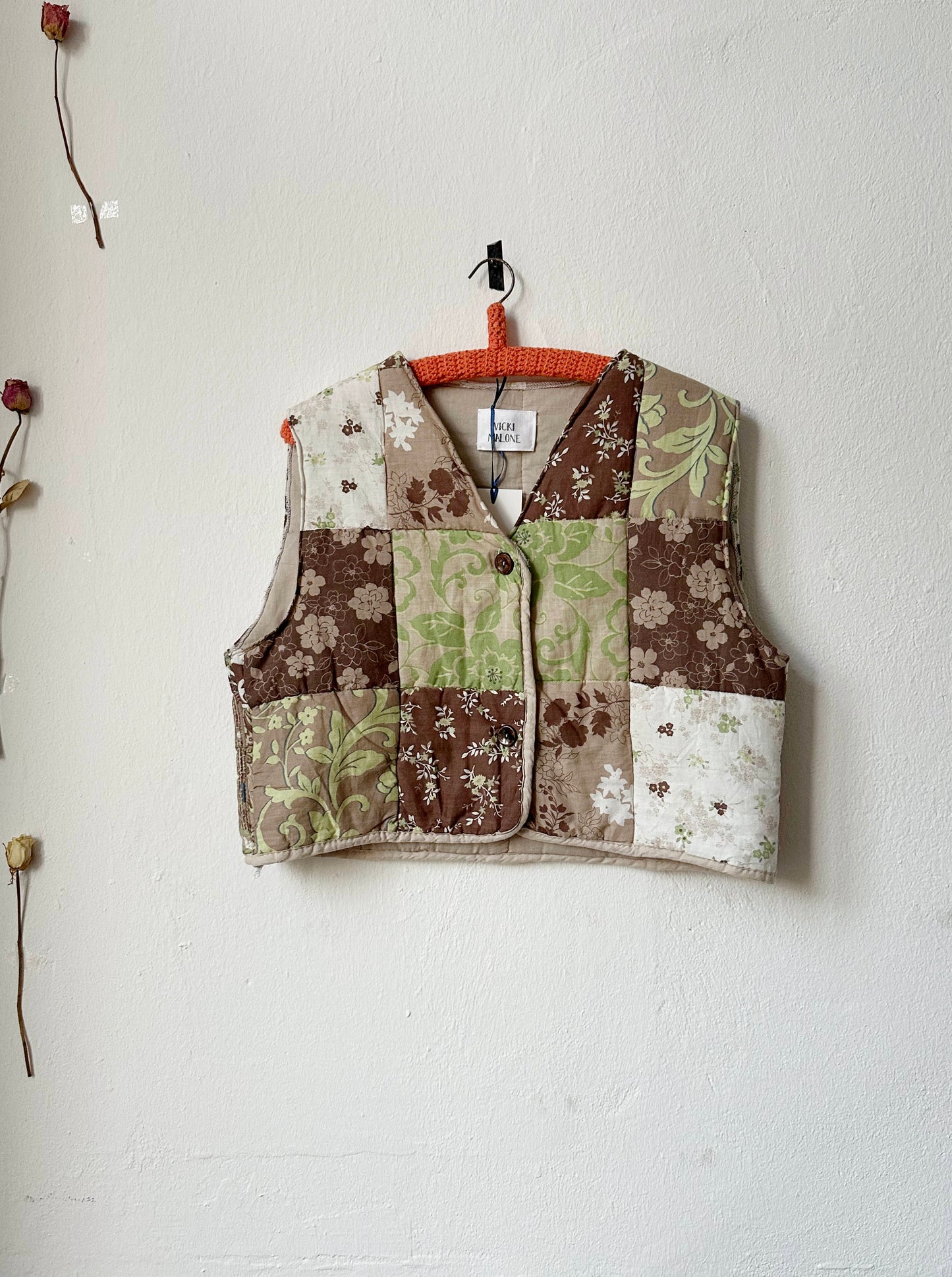 Quilted vest with button front fastening, displayed on a hanger against a neutral background.