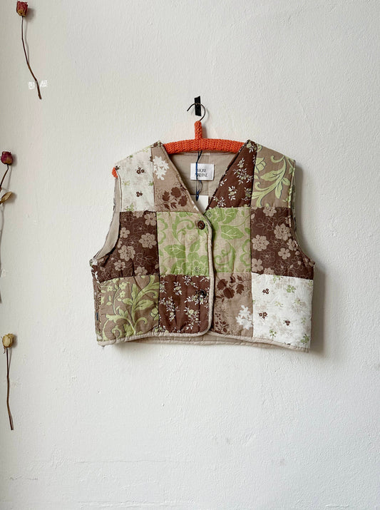 Quilted vest with button front fastening, displayed on a hanger against a neutral background.