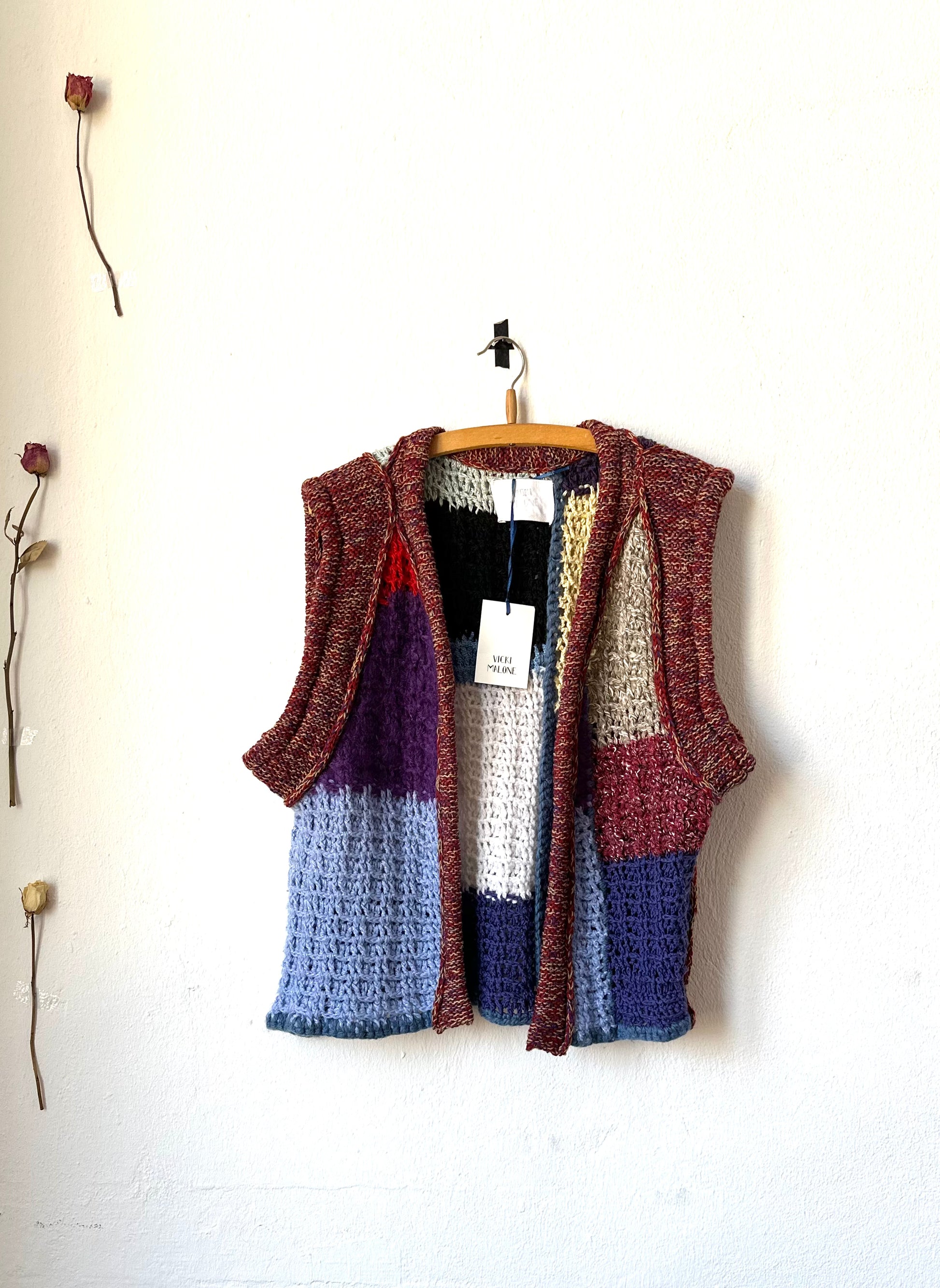 A colour blocked crochet vest hangs on a wall
