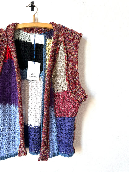 A detail view of the front of a colour blocked crochet vest hanging on a wall.
