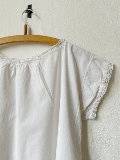 White vintage dress with lace trim on a wooden hanger against a white wall