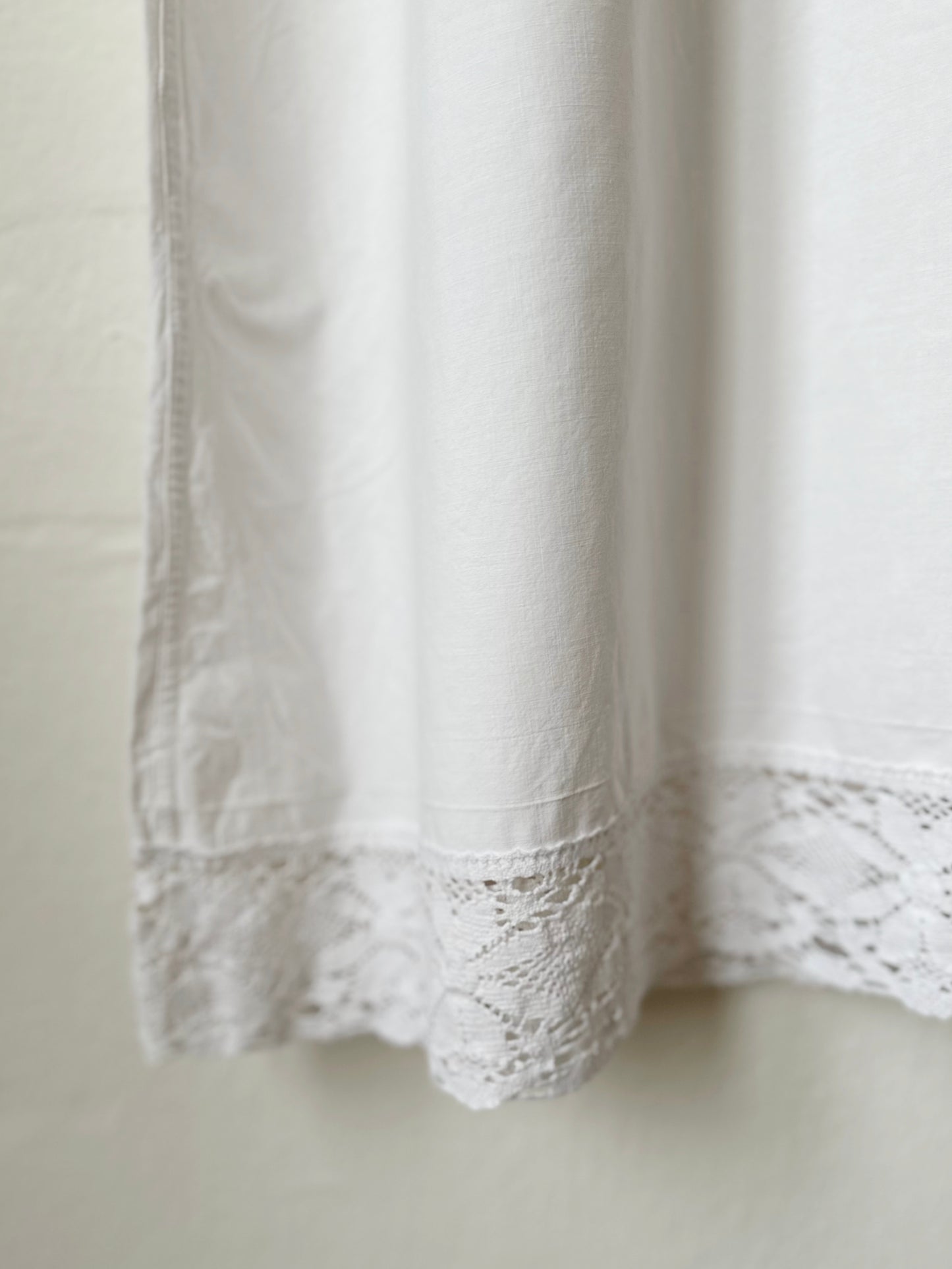White lace hem detail of a dress hanging on a plain background